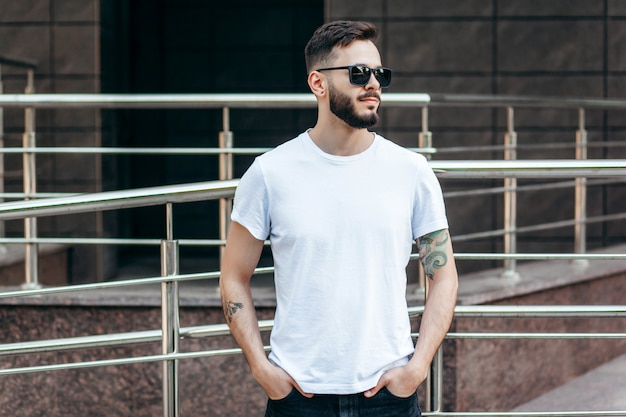 Ein junger stilvoller Mann mit einem Bart in einem weißen T-Shirt und einer Sonnenbrille