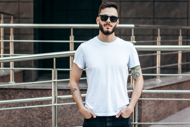 Ein junger stilvoller Mann mit einem Bart in einem weißen T-Shirt und einer Sonnenbrille