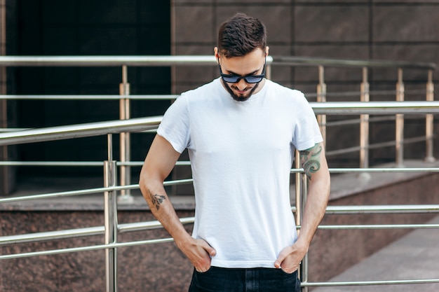 Ein junger stilvoller Mann mit einem Bart in einem weißen T-Shirt und einer Sonnenbrille