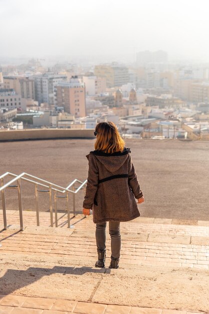 Ein junger Tourist auf der Treppe des Aussichtspunkts Cerro San Cristobal und der Stadt Almeria im Hintergrund, Andalusien. Spanien. Costa del Sol im Mittelmeer, vertikales Foto