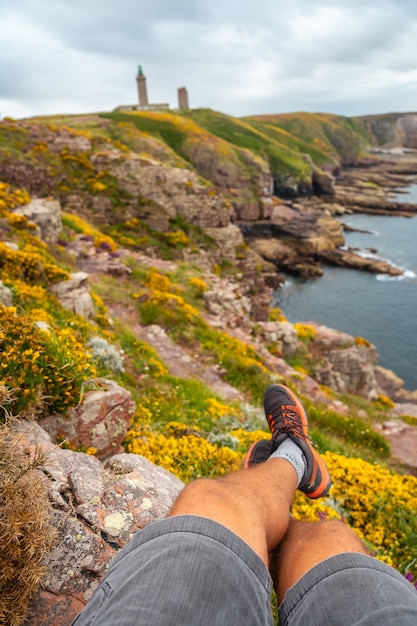 Ein junger Tourist, der an der Küste neben dem Phare Du Cap Frehel sitzt, ist ein maritimer Leuchtturm in Cotes-dÃƒÂ'Ã'Â´Armor (Frankreich). An der Spitze des Cap Frehel