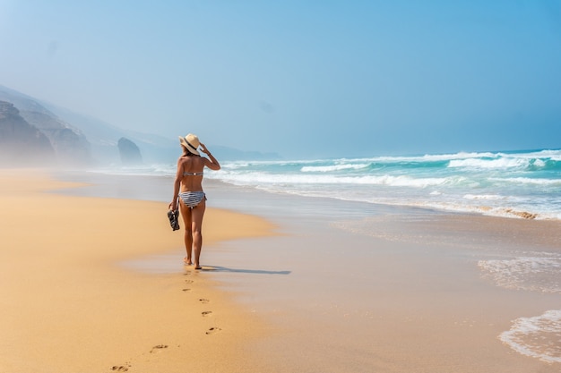 Ein junger Tourist mit Hut allein zu Fuß am Strand von Cofete des Naturparks Jandia, Barlovento, südlich von Fuerteventura, Kanarische Inseln. Spanien