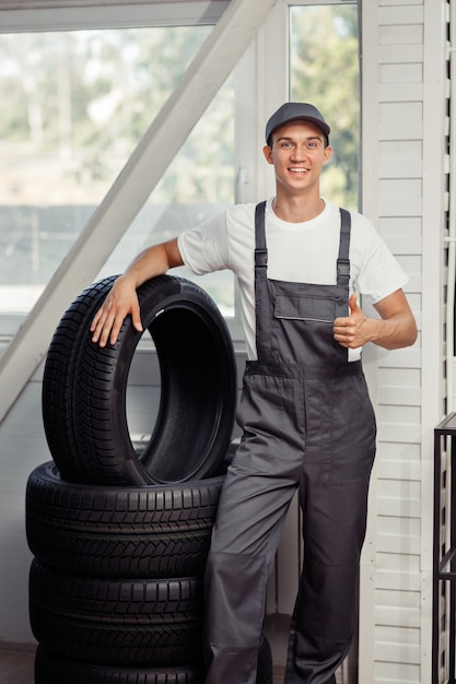 Ein junger und attraktiver Automechaniker steht bei der Arbeit neben mehreren Autoreifen.