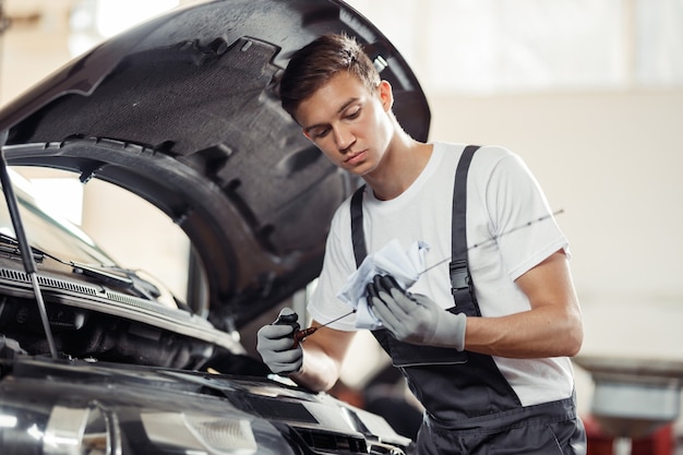 Ein junger und attraktiver Mechaniker überprüft den Ölstand eines Automotors.