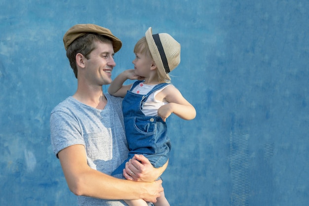 Ein junger Vater hält seine Tochter auf seinen Händen Blauer Hintergrund Kopieren Sie Platz