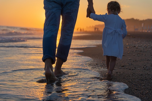 Ein junger Vater mit einer kleinen Tochter geht im Sonnenuntergang am Meeresstrand entlang