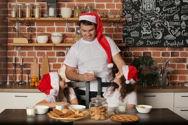 Ein junger Vater mit Weihnachtsmannmütze in der Küche steht neben seinen beiden Töchtern