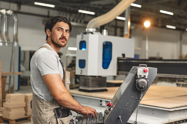 Ein junger Zimmermann bedient eine Holzverarbeitungsmaschine in einer Möbelfabrik