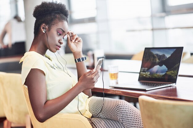 Ein junges Afroamerikanermädchen mit dem dunklen gelockten Haar einen Laptop in einem Café erwägend