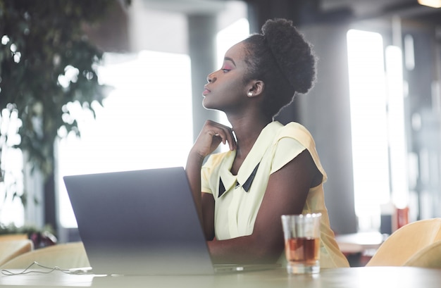 Ein junges afroamerikanisches Mädchen mit dunklem lockigem Haar, das einen Laptop in einem Café erwägt