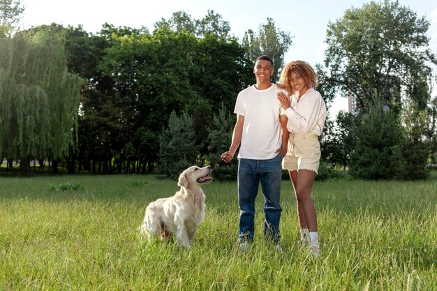 Ein junges afroamerikanisches Paar mit einem Hund steht im Park auf grünem Gras und lächelt