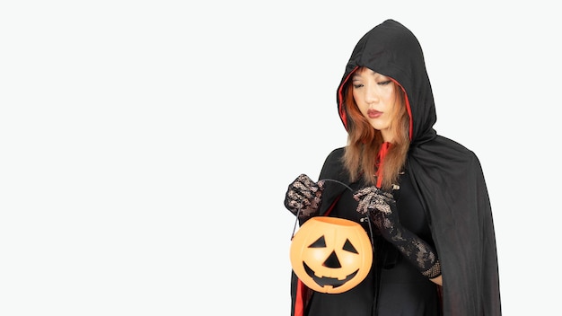 Ein junges asiatisches Mädchen im schwarzen Kleid und in der schwarzen Reithaube hält Kürbis am Halloween-Tag