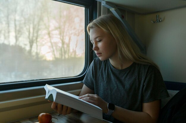 Ein junges blondes Mädchen fährt in einem Zug und liest ein Buch Bildung, Ausbildung und Reisen Closeup