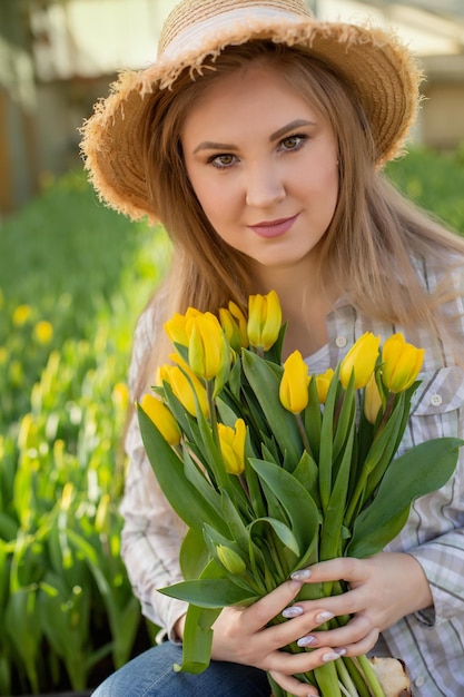 Ein junges blondes Mädchen mit Strohhut hält einen Strauß gelber Tulpen in den Händen