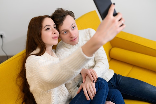 Foto ein junges ehepaar zu hause sitzt auf der couch und macht selfies