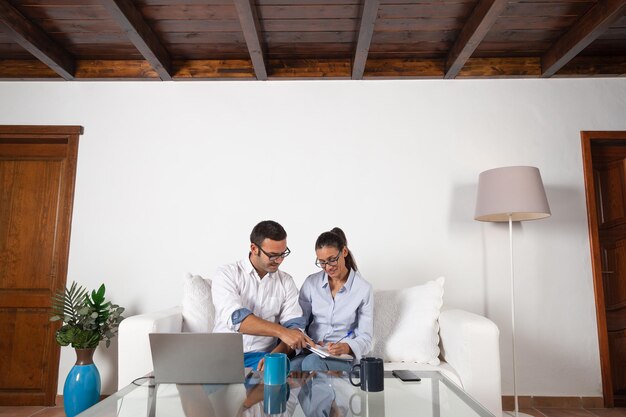 Ein junges erwachsenes Paar nimmt Notizen mit dem Laptop und macht einen Online-Kurs im Wohnzimmer zu Hause