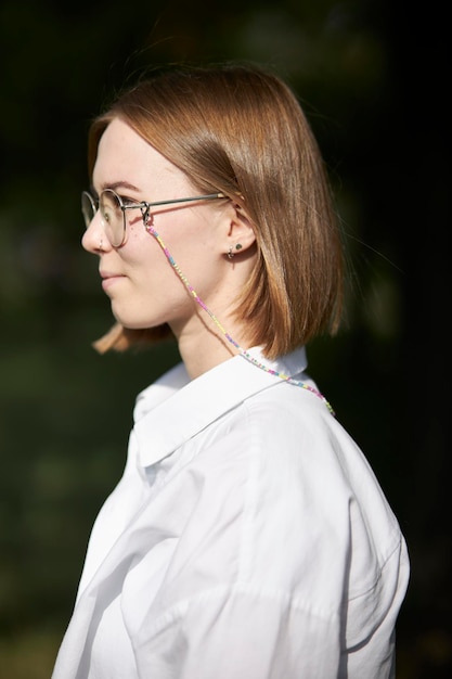 Ein junges europäisches Mädchen mit Brille ruht in einem Park auf einer grünen Daube. Porträt eines Mädchens