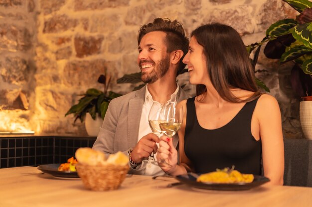 Ein junges europäisches Paar, das beim Abendessen in einem Restaurant auf Getränke röstet und Valentinstag feiert