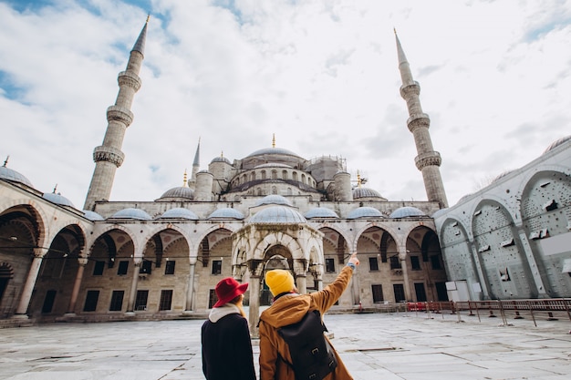 Ein junges europäisches Paar geht in den Hof der Blauen Moschee in Istanbul, Türkei. Reisender Mann und Mädchen in gelben Hüten gehen im Winter Istanbul. bewölkter Herbsttag in Istanbul.