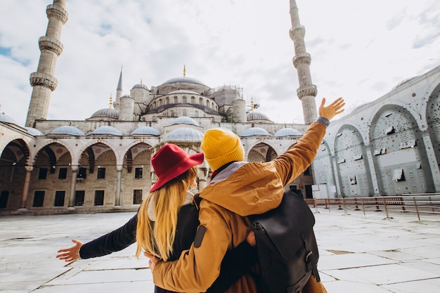 Foto ein junges europäisches paar geht in den hof der blauen moschee in istanbul, türkei. reisender mann und mädchen in gelben hüten gehen im winter istanbul. bewölkter herbsttag in istanbul.