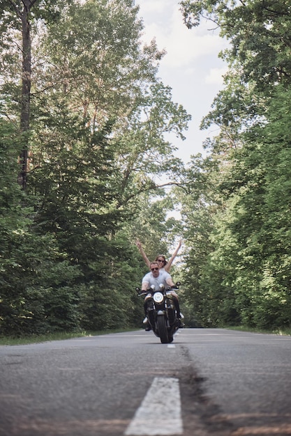 Ein junges glückliches Paar fährt mit dem Motorrad auf einer Asphaltstraße im Wald Freiheit und Geschwindigkeit