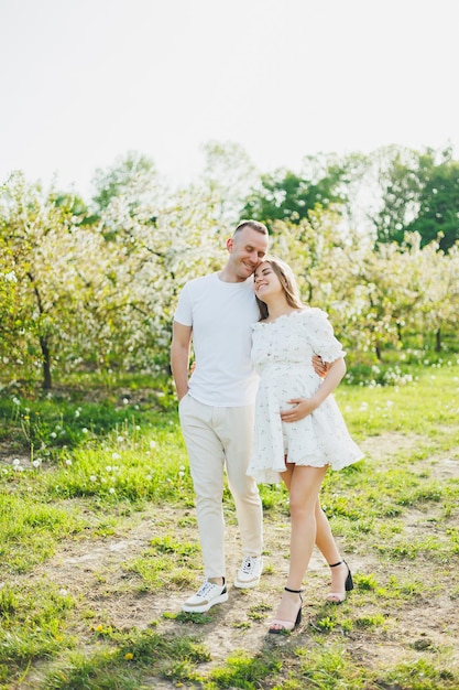 Ein junges glückliches Paar geht in Erwartung einer Schwangerschaft durch einen blühenden Garten. Verliebtes Paar in blühenden Apfelbäumen
