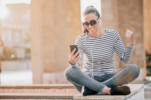 Ein junges, glückliches Teenager-Mädchen, das ein Smartphone in der Stadt benutzt