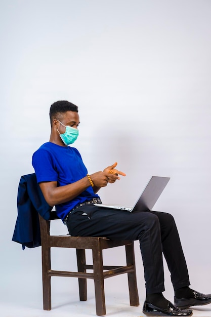 Ein junges, gutaussehendes afrikanisches Unternehmen, das vor weißem Hintergrund isoliert ist und eine Gesichtsmaske trägt, um sich vor dem Ausbruch in der Gesellschaft zu schützen, und ist aufgeregt über das, was er auf seinem Laptop gesehen hat