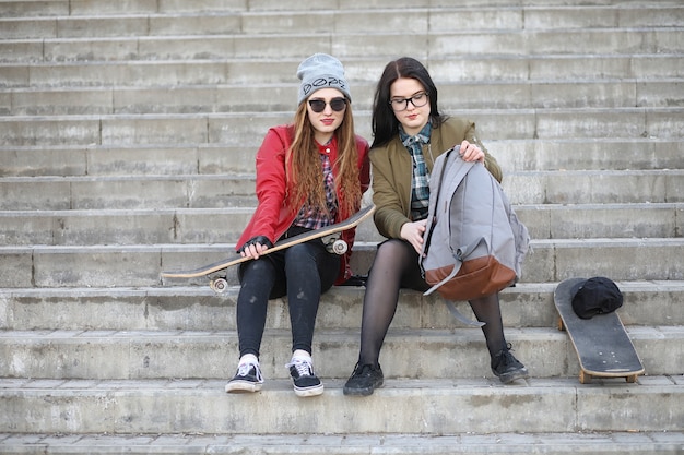 Ein junges Hipster-Mädchen reitet ein Skateboard. Mädchenfreundinnen für einen Spaziergang in der Stadt mit einem Skateboard. Frühlingssport auf der Straße mit einem Skateboard.