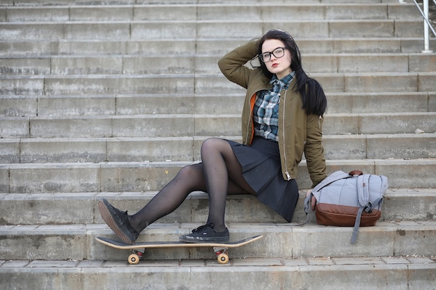 Ein junges Hipster-Mädchen reitet ein Skateboard. Mädchenfreundinnen für einen Spaziergang in der Stadt mit einem Skateboard. Frühlingssport auf der Straße mit einem Skateboard.