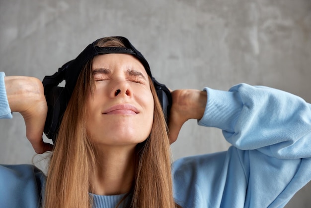 Ein junges, hübsches, langhaariges Mädchen in einem blauen Pullover, einer schwarzen Baseballkappe und schwarzen Kopfhörern hört zu