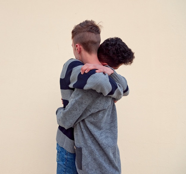 Ein junges interracial schwules Paar umarmt sich isoliert auf einem beigen Hintergrund