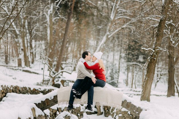 Ein junges Liebespaar in Winterjacken und -schals, die in einem Schneepark sitzen