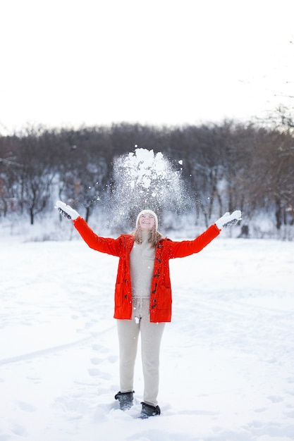 Ein junges Mädchen, blond, in Pullover, Mütze und orangefarbener Jacke, vor dem Hintergrund der Winterlandschaft. Schnee und Frost, das Konzept von Weihnachten.