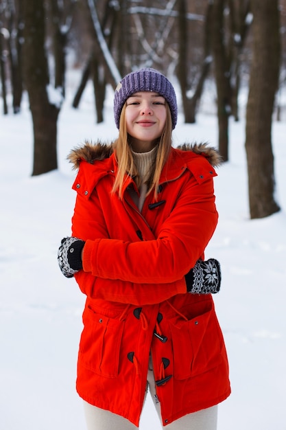 Ein junges Mädchen, blond, in Pullover, Mütze und orangefarbener Jacke, vor dem Hintergrund der Winterlandschaft. Schnee und Frost, das Konzept von Weihnachten.