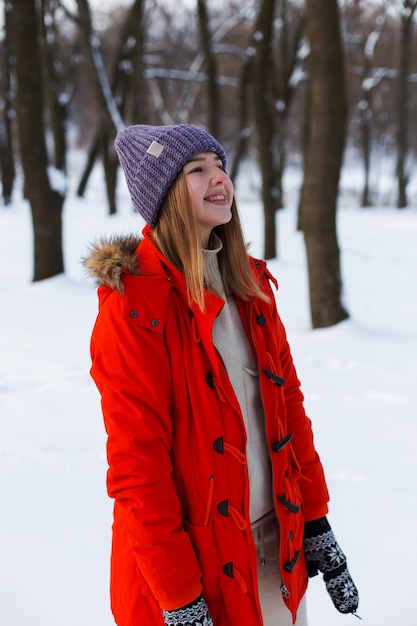 Ein junges Mädchen, blond, in Pullover, Mütze und orangefarbener Jacke, vor dem Hintergrund der Winterlandschaft. Schnee und Frost, das Konzept von Weihnachten.