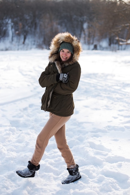 Ein junges Mädchen, brünett, in Pullover, Hut und grüner Jacke, vor dem Hintergrund der Winterlandschaft. Schnee und Frost, das Konzept von Weihnachten.