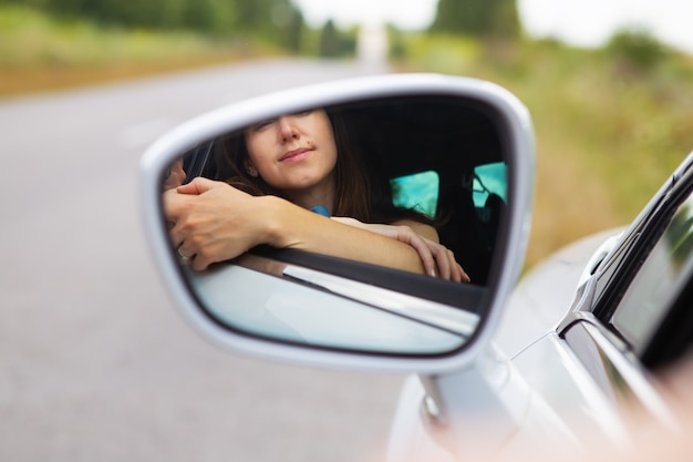 Ein junges Mädchen, das ein Auto fährt, das Mädchen schaut in den Seitenspiegel. Lieferung für das Recht, ein Auto zu fahren.