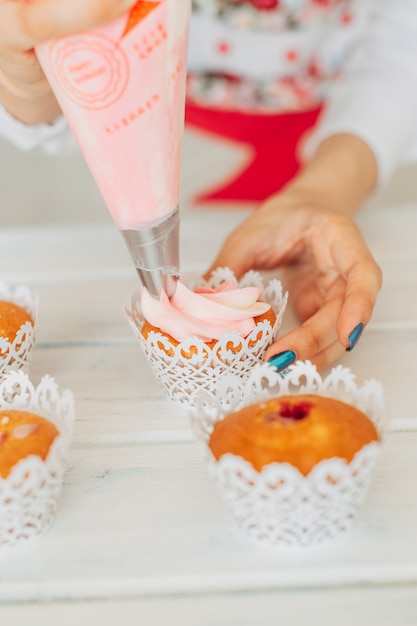 Ein junges Mädchen dekoriert Cupcakes mit Sahne.