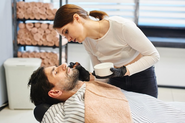 Ein junges Mädchen Friseur rasiert sich den Bart, der Mann im Friseurladen