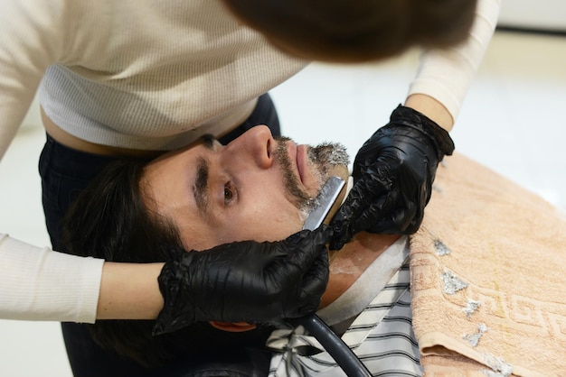 Foto ein junges mädchen friseur rasiert sich den bart, der mann im friseurladen