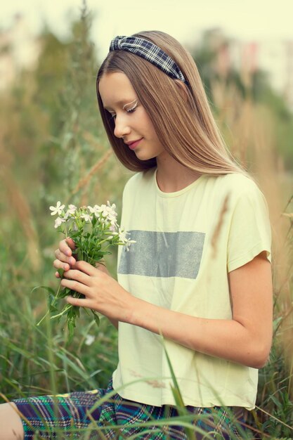 Ein junges Mädchen hält einen Haufen Wildblumen in ihren Händen Nettes Mädchen mit langen Haaren auf der Wiese