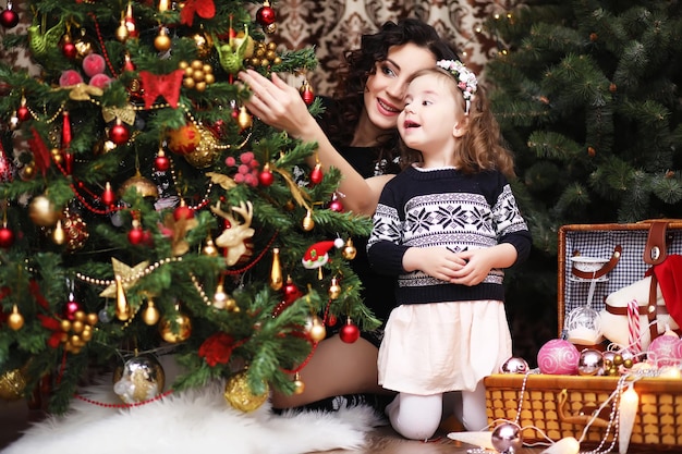 Ein junges Mädchen hilft ihrer Mutter, den Weihnachtsbaum der Familie zu schmücken. Familien-, Winterferien- und Menschenkonzept - glückliche Mutter und kleine Tochter zu Hause.