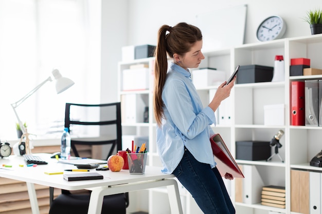 Ein junges Mädchen im Büro steht auf einem Tisch und hält ein Telefon und einen Ordner in der Hand