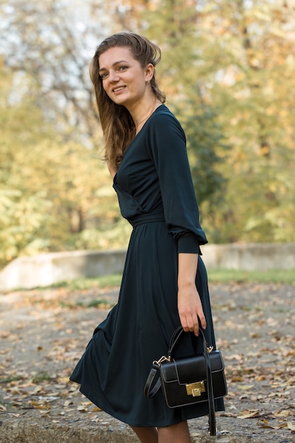 Ein junges Mädchen im Kleid wirft in einem Park auf einem Hintergrund des goldenen Herbstlaubs auf.