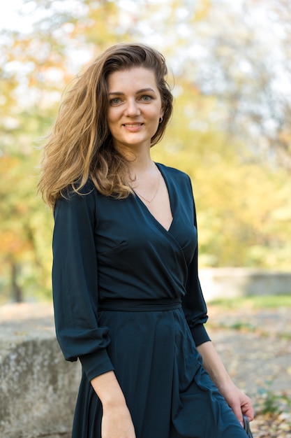 Ein junges Mädchen im Kleid wirft in einem Park auf einem Hintergrund des goldenen Herbstlaubs auf.