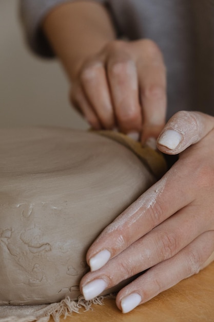 Ein junges Mädchen in einem grauen langen Ärmel stellt in einer Bildhauerwerkstatt mit ihren eigenen Händen eine Tonvase her