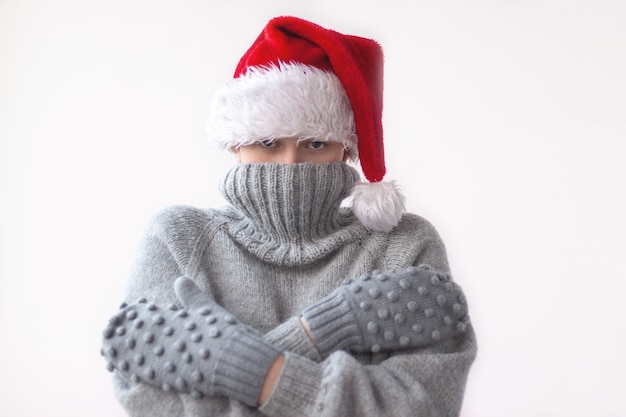 Ein junges Mädchen in einem grauen Strickpullover, Handschuhen und einer roten Weihnachtsmütze zog den Kragen des Pullovers über ihr Gesicht und umarmte sich