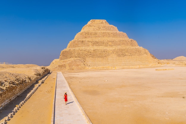 Ein junges Mädchen in einem roten Kleid, das in der Stufenpyramide von Djoser, Saqqara geht. Ägypten. Die wichtigste Nekropole in Memphis. Die erste Pyramide der Welt