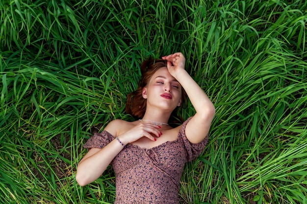 Ein junges Mädchen in einem schönen Kleid liegt im grünen Gras